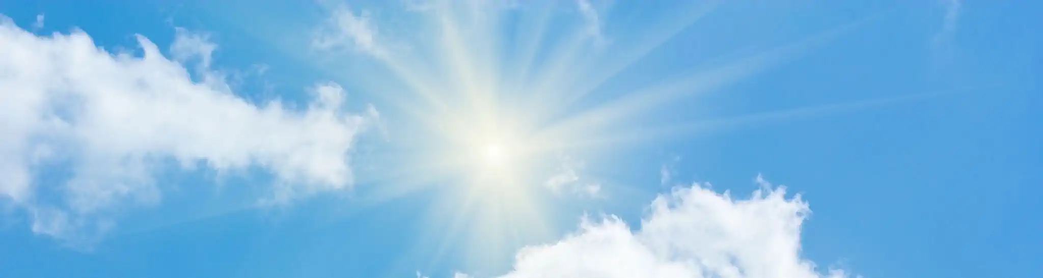 Image of the sun shining between billowy white clouds in a blue sky